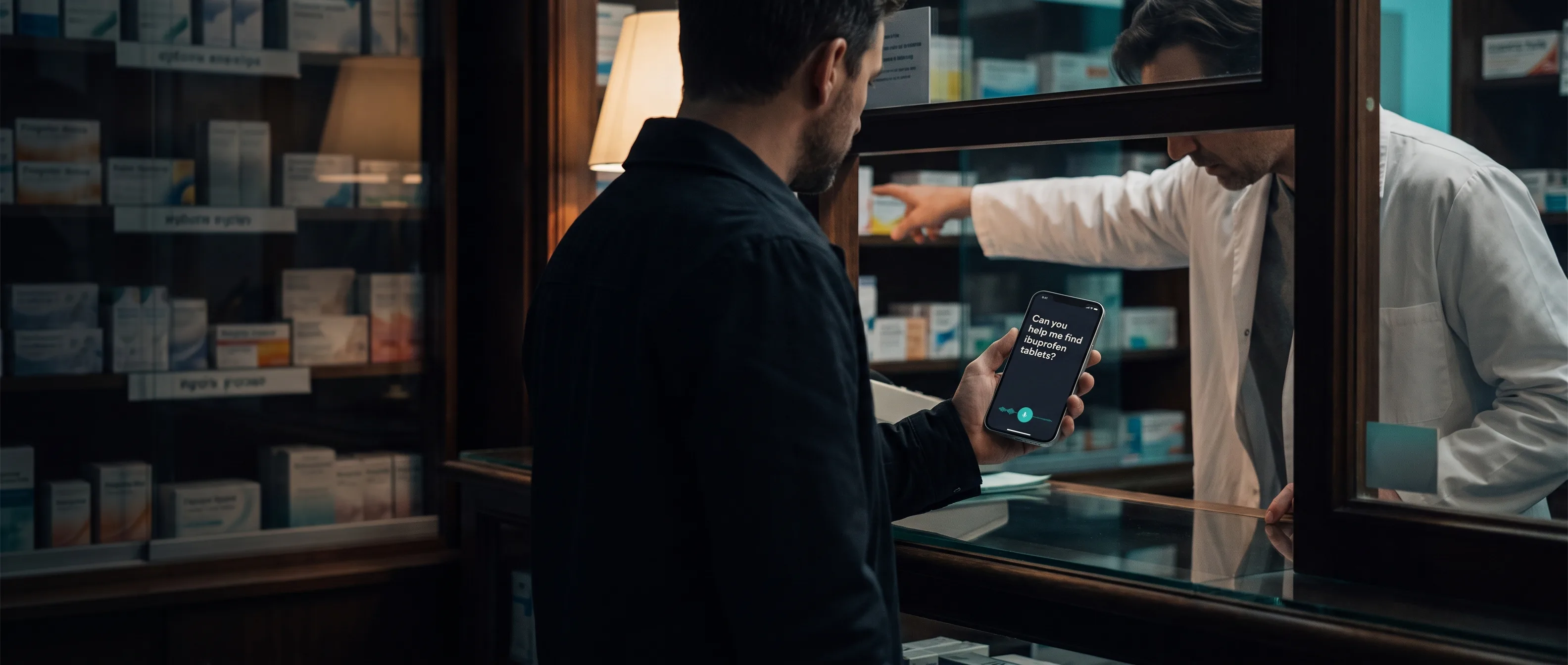 A traveler at a pharmacy counter holds up a phone showing a clearly phrased request card while the pharmacist leans in to read it.